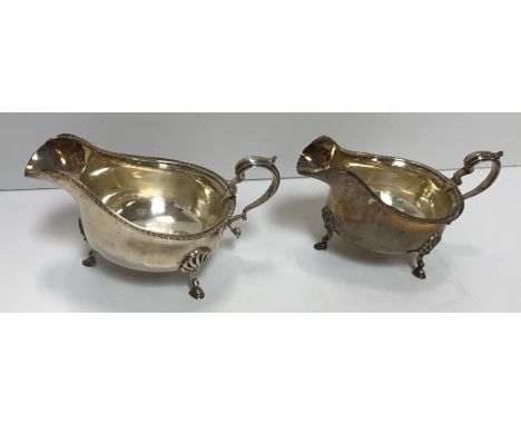 A pair of George V silver sauceboats with gadrooned edge, raised on three hoof feet and with scrolling handle (by Goldsmiths 
