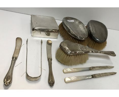 A collection of silver wares to include two silver mounted hairbrushes, a pair of silver sugar tongs, two silver bladed mothe