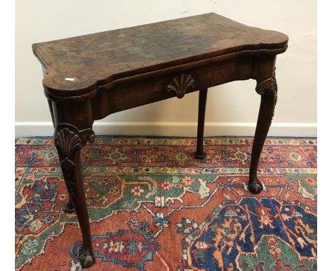 An 18th Century walnut veneered card table, the shaped top quartered, cross banded and feather strung over a recessed frieze 