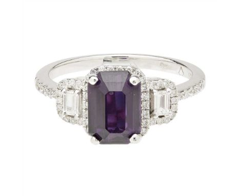 A purple sapphire and diamond set ring claw set with a deep pinkish-purple emerald-cut sapphire, in a border of small round b