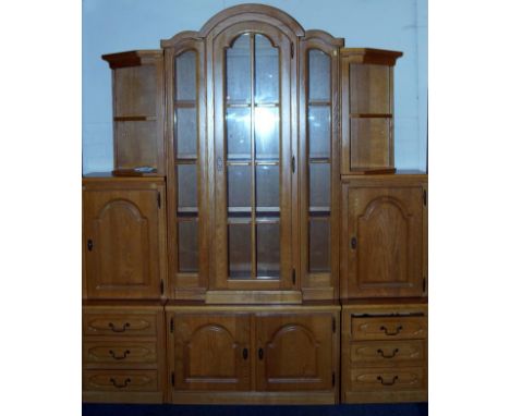 An oak display cabinet, in three vertical sections, the centre section with a glazed door flanked by glazed sections with the