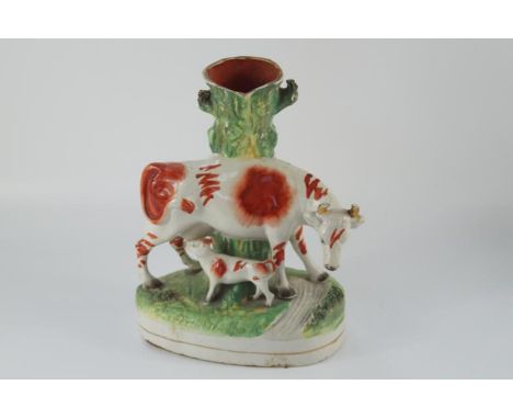 A 19thC Staffordshire figure group, of a cow and calf, moulded with a tree trunk, on a rustic base, 29cm high.