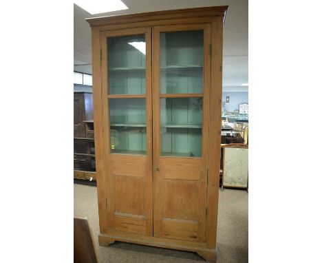 A 20th Century limed stripped pine bookcase, the projecting cornice above a pair of glazed and panelled doors enclosing shelv