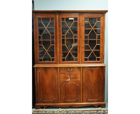 A 20th Century mahogany bookcase, the projecting dentil moulded cornice above three astragal glazed doors enclosing adjustabl