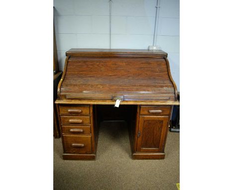 An early 20th Century oak roll top desk, the rectangular top above a tambour front enclosing an arrangement of drawers and pi