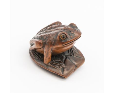 A 19th century Japanese wooden frog netsuke, perching on a leaf with orange eyes, signed underneath, approx. 3cm high x 3.4cm