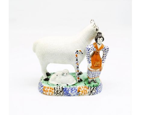 A Prattware model of a sheep and her lambs laying beneath her, with a shepherdess standing to the side, sponge decorated in b