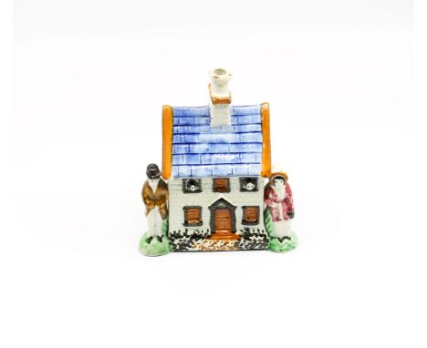 A small Prattware money box in the shape of a house, flanked with a man and woman on either side. Decorated in ochre, blue, g