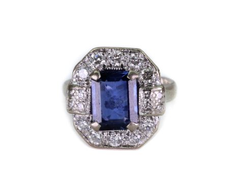 A white gold, sapphire and diamond cluster ring, the central octagonal cut sapphire claw set between two diamond set panels a