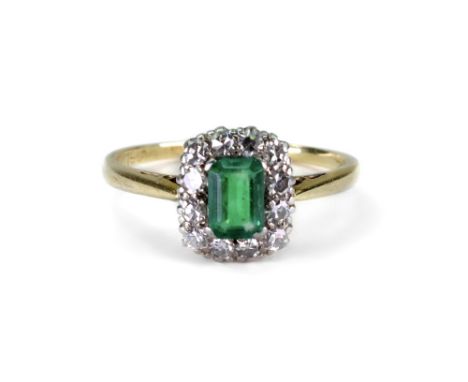 An emerald and diamond rectangular cluster ring, early 20th century, the step-cut emerald four-claw set within a twelve-stone