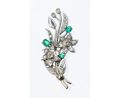 A diamond and emerald spray 18ct white gold  brooch, comprising two daisy heads each one rub over set to the centre with a ro