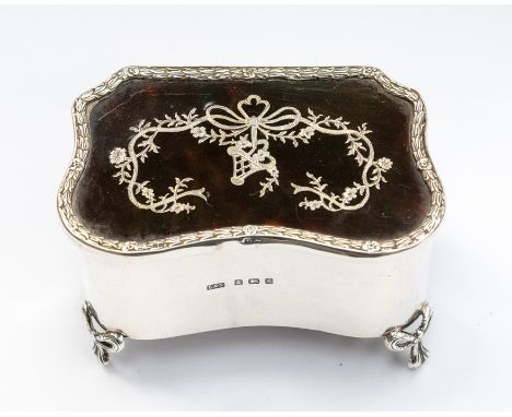 An Edwardian silver and tortoiseshell serpentine shaped ring box, the cover with husk and flower border with inlaid ribbon ti