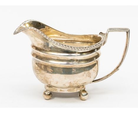 An early 19th Century silver helmet shaped cream jug, gadrooned border above plain body engraved with initials, on four ball 