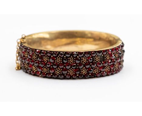 A Victorian Bohemian garnet and gilt metal bangle, comprising round cut garnets and gilt cluster arrangements, width approx 1