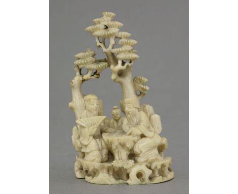 An ivory figure Group,19th century, of two figures playing Go, whilst a child looks on, backed by rockwork and beneath pine t