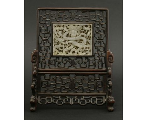 A small jade Table Screen,19th century, carved with a writhing dragon amongst clouds, mounted in a pierced hongmu stand, 18.5