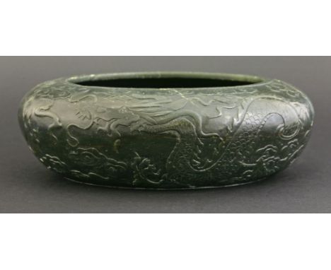 A spinach-green jade Alms Bowl,18th/19th century, the exterior carved with a complex low relief scene of two dragons amongst 