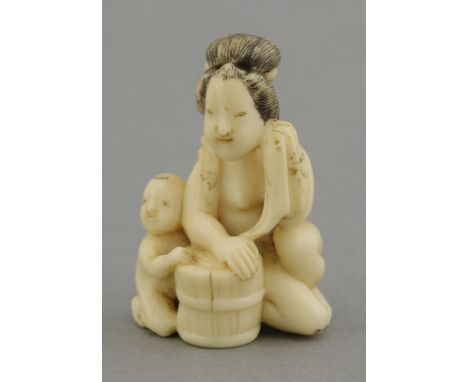 An attractive ivory Netsuke,mid-19th century, of a bare-breasted woman about to bathe her child in a bucket, her hair black-s