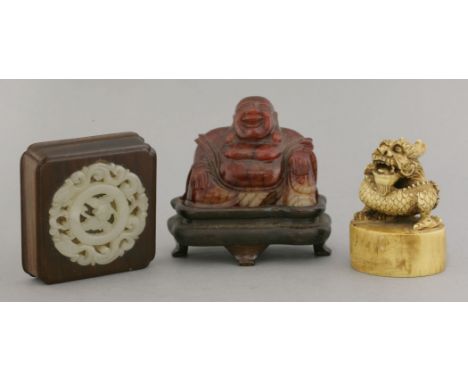 A pierced jade disc, set into a wood paperweight, 7cm, an ivory seal, the knop a curled dragon, 7cm, and a stained soapstone 