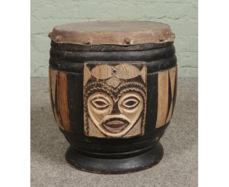 A carved tribal drum with mask decoration and hide skin. Height 39cm.