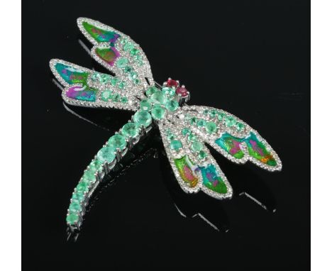 A silver and enamel dragonfly brooch. Set with ruby eyes, and emeralds and diamonds to the body and wings. Emeralds 3.5ct, di