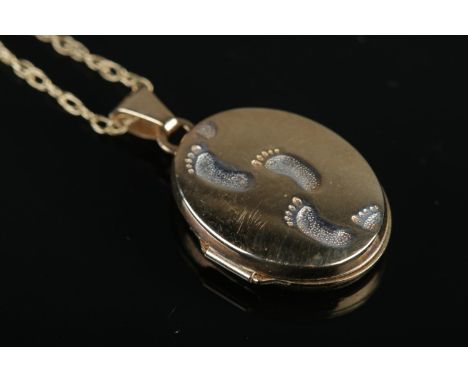 A 9ct Gold locket bearing footprints to the front, suspended on dainty 9ct Gold necklace chain. The back of the locket with i
