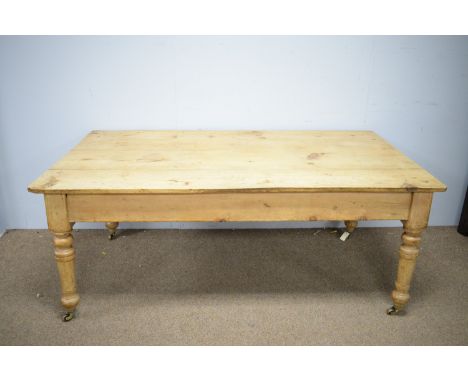 A 20th Century pine dining table, the shaped top raised on ring turned legs, raised on castors, 72.5 x 179 x 101.5cms.