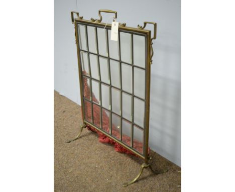 An early 20th Century brass and glazed firescreen, with 24 leaded glass panels, enclosed by brass surround, raised on outswep