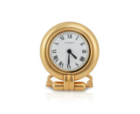 A Cartier brass travel alarm clock. The clock having a white face and roman numerals with two cabochon sapphire winders to ba