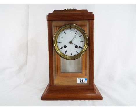 A glass and wood cased mantel clock, the French round plate movement striking hour and half past on a bell, white enamel dial