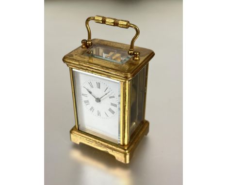 A modern brass four glass clock with folding carry handle to top white enamel dial with roman numerals raised on bracket feet