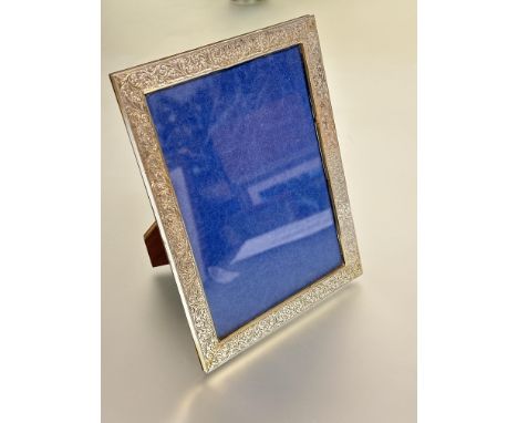 A 1920s silver rectangular photograph frame with chased scrolling acanthus leaf design and early plastic mount and mahogany b