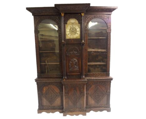 A 17TH CENTURY STYLE OAK BREAKFRONT DISPLAY CABINET the carved overhanging cornice above a brass dial to Phil Walton, Devises