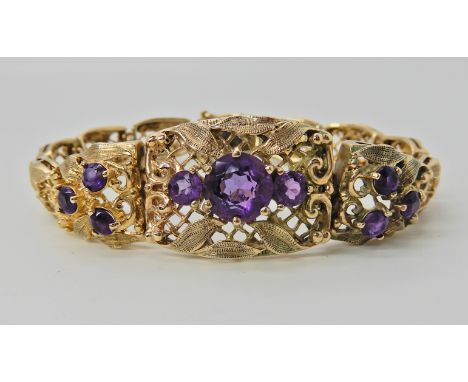 A 9CT GOLD AMETHYST SET BRACELET with pierced scroll and leaf design panels tapering to the back to a box clasp with safety c