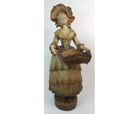 A GOLDSCHEIDER PAINTED TERRACOTTA FIGURE OF A WOMAN in crinoline dress and bonnet holding a basket, impressed and applied mar