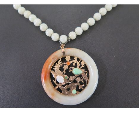 A green hardstone necklace - Suspending an openwork gem-set pendant, depicting birds - Stamped 14K - Length of necklace 70cms