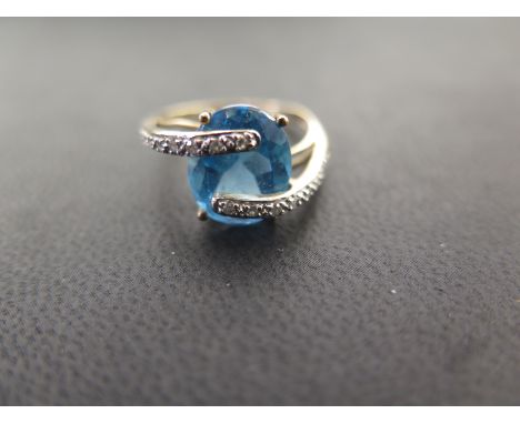 A 9ct gold blue-gem and diamond crossover style ring - Believed to be topaz - Hallmarked London - Ring size R - Weight approx