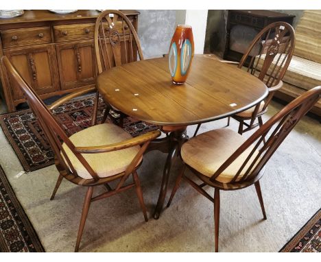 Vintage elm Ercol extending table on quatrefoil  base, together with a set of four elm Ercol Swan back hoop and spindle chair
