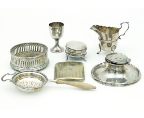 A silver capstan inkwell, Birmingham 1910, a cream jug, an egg cup, a bottle coaster, a strainer, a cigarette case and a ring