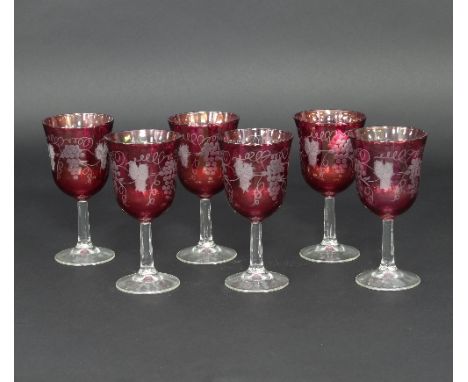 Six ruby tinted glasses, etched grapes and vines on plain stems with circular bases, 16cm high