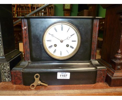 A black slate Mantle clock with red details, having white enamel face, Roman numerals, two chimes, key and pendulum, 12" wide