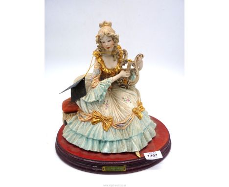 A porcelain figure of a lady in period dress playing a harp, 12 1/2" wide x 12" tall.