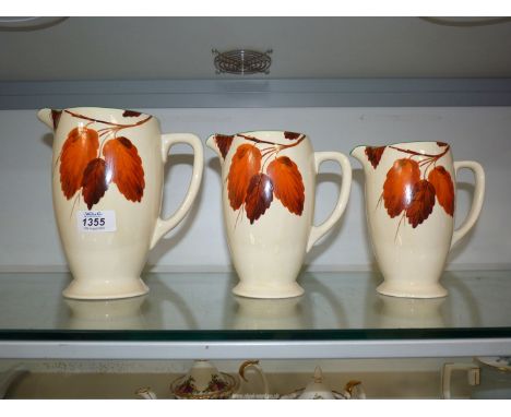 Three graduated 'Autumn leaves' jugs, (small chips to rims), by Clarice Cliff for J. Wilkinson Art.