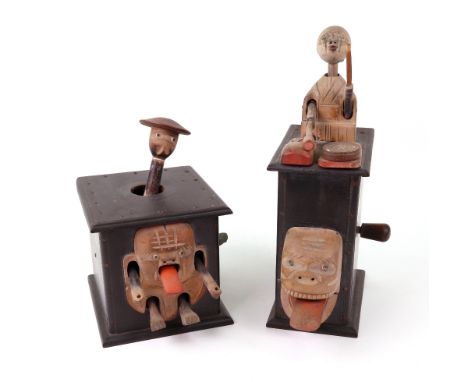 Two carved wooden Japanese Kobi toys; one with a man on top of a wooden box playing a drum, with a grotesque face mounted to 