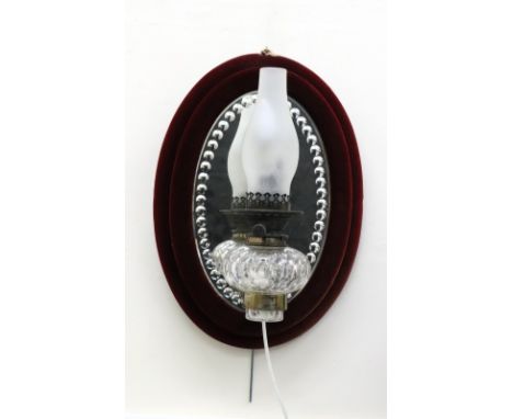 A late Victorian oval wall mirror, with claret plush velvet covered frame and fitted with a facet cut glass oil lamp, Hinks's