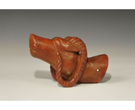 An undated archaistic red stone finial in the form of a ram's head with lentoid eyes and c-shaped horns; the neck hollow to t