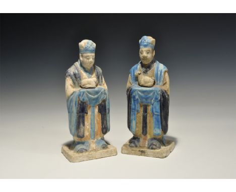 An undated archaistic pair of glazed ceramic figurines in Ming Dynasty, 1368-1644 AD style comprising: one standing on a rect