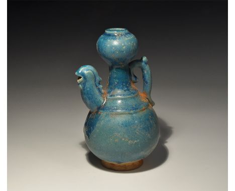An undated archaistic blue-glazed ceramic jug with tall balustered neck and bulb, scrolled handle with thumb-pad, spout forme