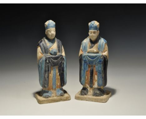 An undated archaistic pair of glazed ceramic figurines in Ming Dynasty, 1368-1644 AD style comprising: one standing on a rect