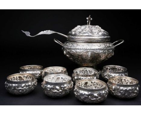 A Burmese silver punch set, 20th century, the cover with an elephant finial, decorated with embossed figures and scrolling fl